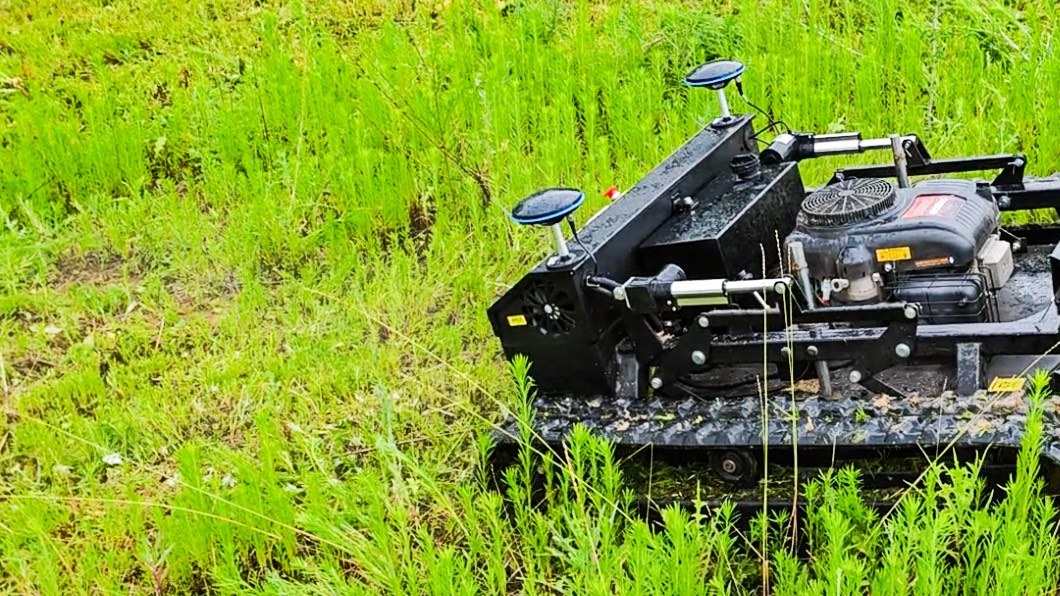Close view of the tracked flail mower deck and drive tracks working in dense green vegetation
