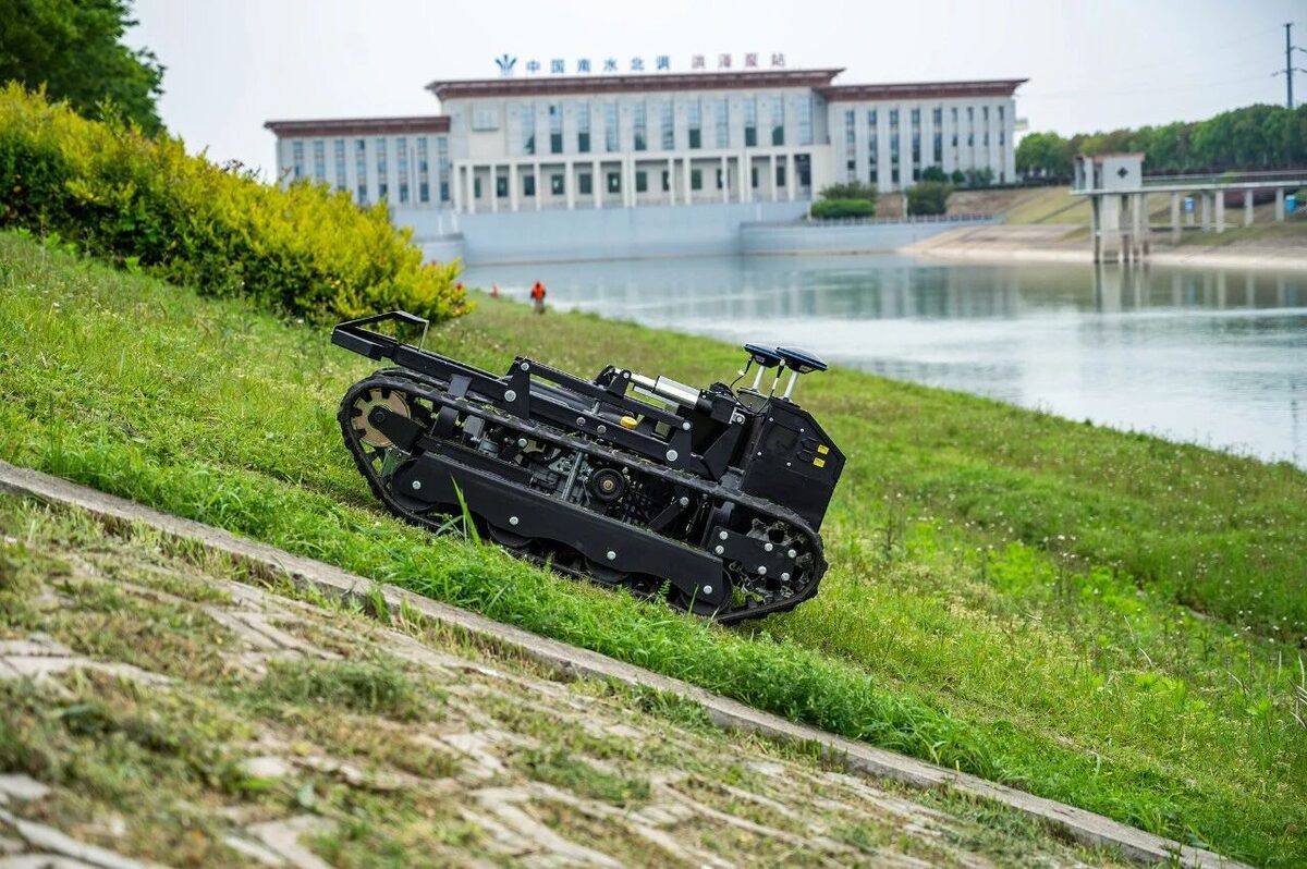 Tracked autonomous mower working on a grassy reservoir embankment beside the water